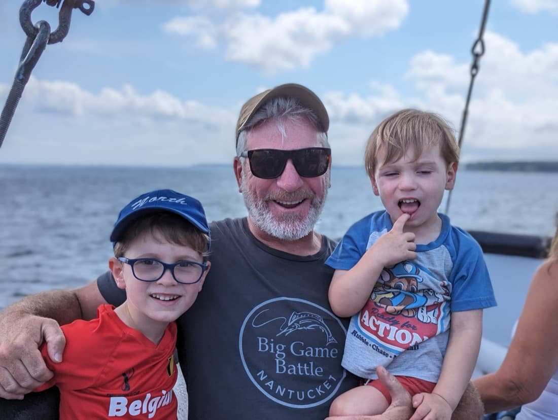 Dan Hermann on the boat with two of his boys, one in glasses and a blue cap, one in his arms