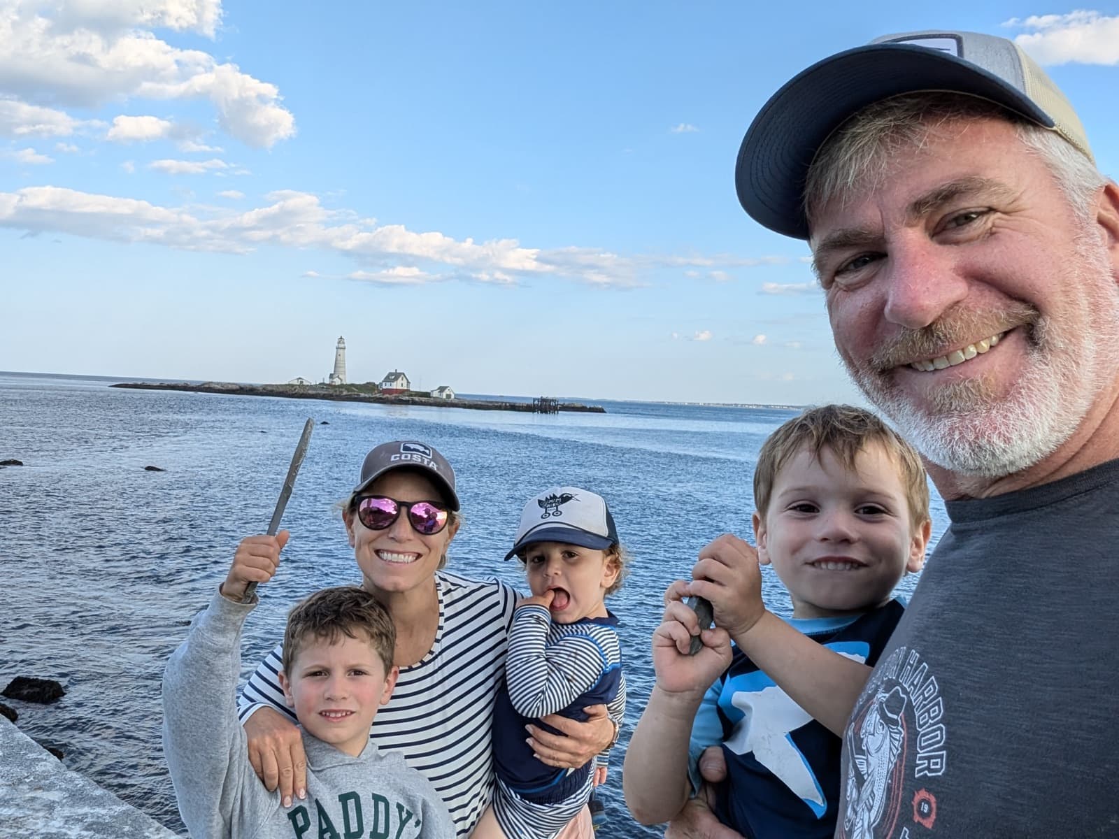 Dan Hermann with his wife and three boys on the rocks in Boston Harbor, Boston Light behind them